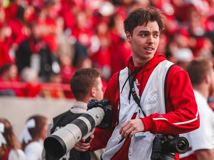 Student wearing reflective vest and holding camera on field at Memorial Stadium