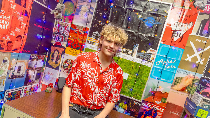 Student in red Hawaiian shirt sitting in room covered with band posters