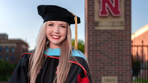Dr. Amy Barry in her regalia in front of the N gate