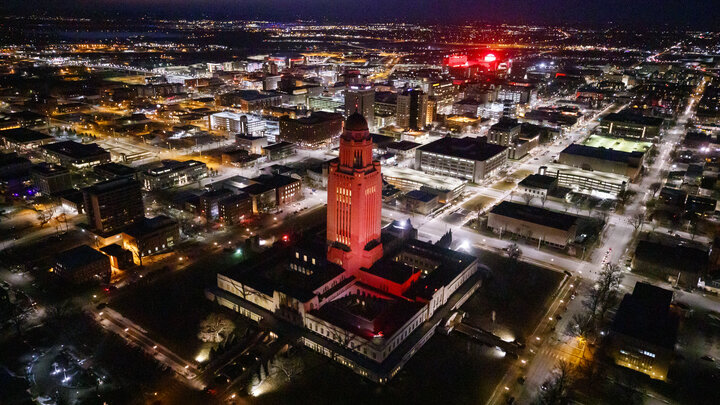 The Nebraska State Capitol shines red with Memorial Stadium and City Campus in the background.