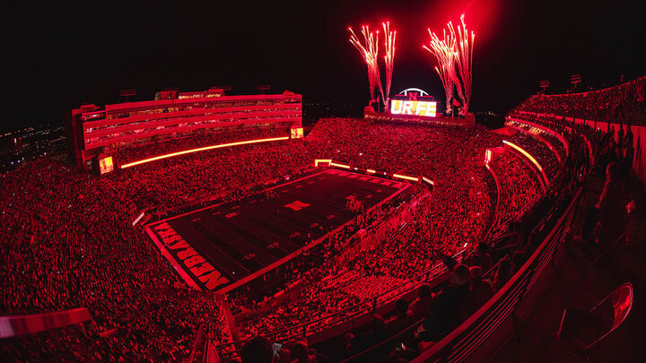 Memorial Stadium during night game, bathed in red light, with fireworks going off near north big screen