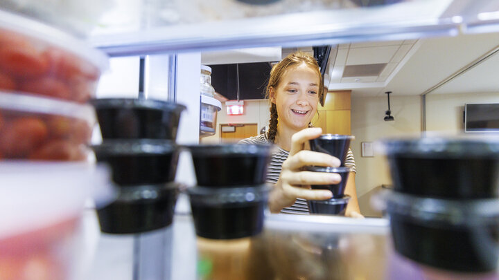 Brenna Mazour, a senior in psychology and dietetics, rearranges containers of shredded cheese in the wellness kitchen refrigerator.  The refrigerated items will be added to the kits when the meals are picked up.