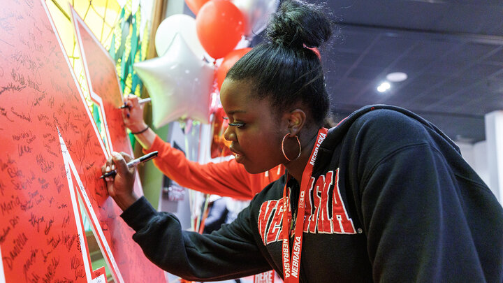 A student wearing a black sweater with a red "Nebraska" across it signs her name on a giant "N" during Admitted Students Day on March 29.