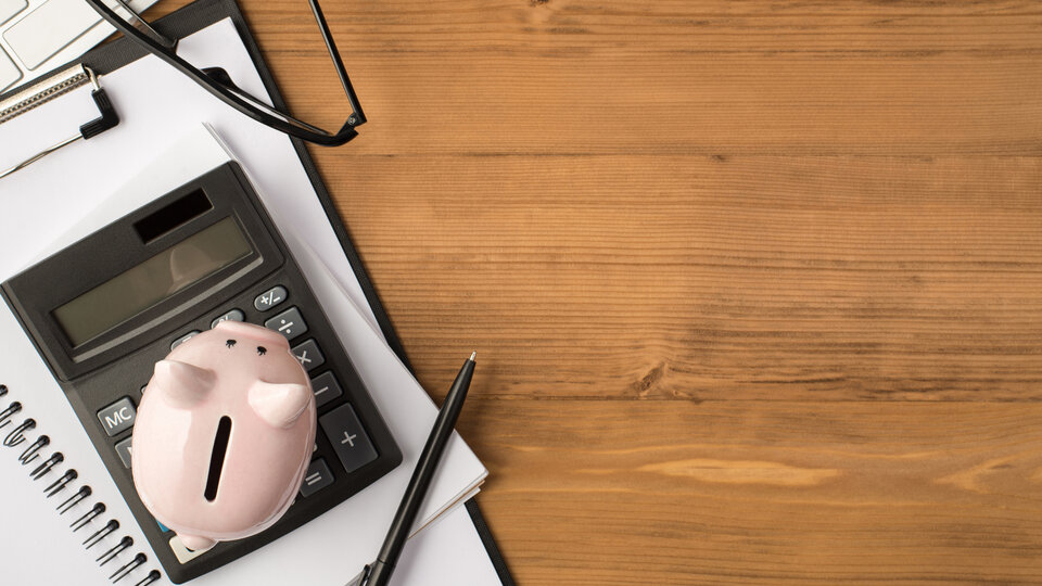 piggy bank on calculator with pen and glasses on table