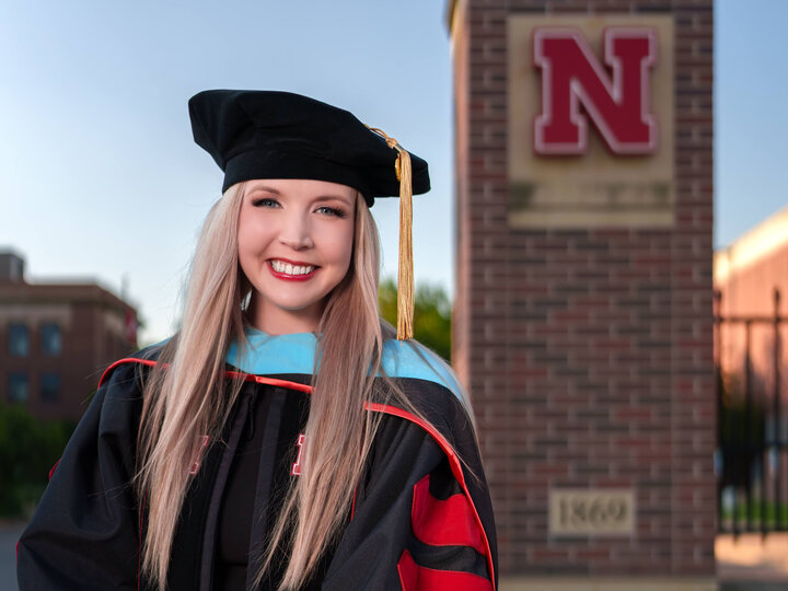 Dr. Amy Barry in her regalia in front of the N gate