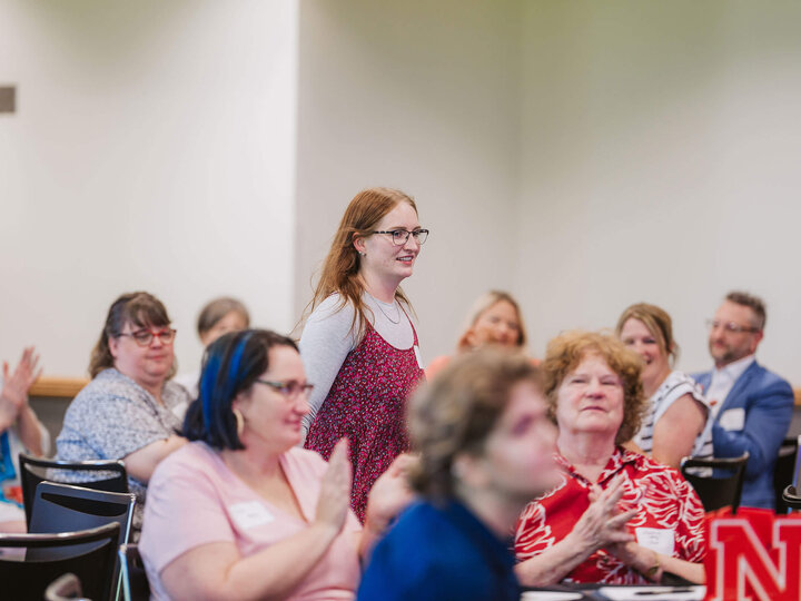 Staff member standing in audience while others clap for her